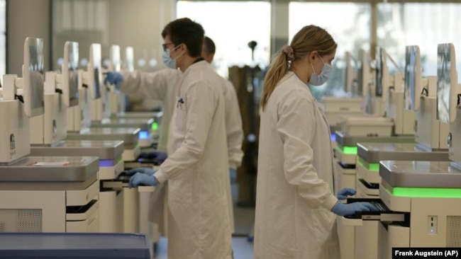 Research assistants watch the sequencing machines analyzing the genetic material of COVID-19 cases at the Wellcome Sanger Institute, Genome Campus, Hinxton, Cambridgeshire, England, Friday, on Jan. 7, 2022. (AP Photo/Frank Augstein)