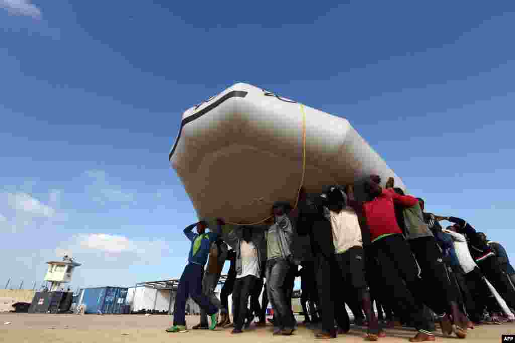 Para migran membawa sebuah perahu, setelah diselamatkan oleh penjaga pantai Libya, di sebuah pangkalan angkatan laut dekat ibukota Tripoli, Libya. Mayat 85 migran yang ditemukan terdampar di pesisir Libya, titik keberangkatan utama untuk menyeberangi laut menuju Eropa, menurut organisasi Bulan Sabit Merah.