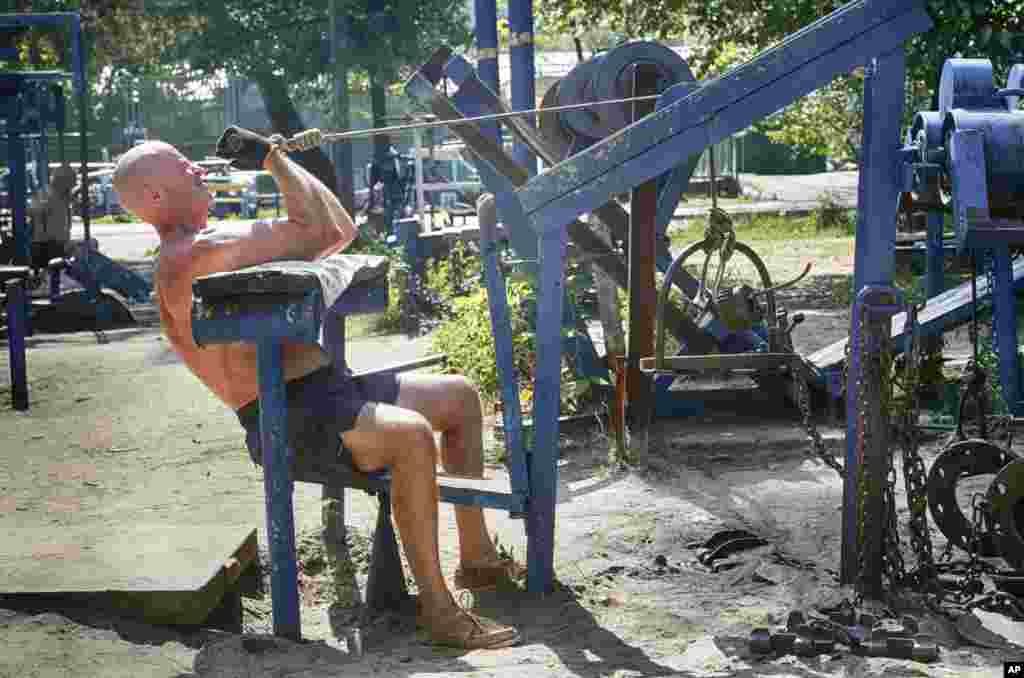 A man lifts metal weights under severe sun in a scrap metal outdoor gym in a city park on the Dnipro river bank in Ukraine's capital Kyiv.
