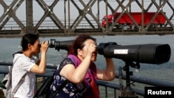 中国游客在辽宁省丹东市跨越鸭绿江的友谊桥边通过望远镜遥望朝鲜。（2018年5月24日）