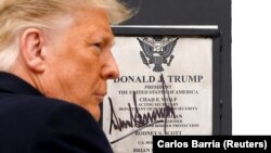 Presiden Donald Trump menandatangani plakat yang dipasang di tembok perbatasan AS-Meksiko dalam lawatan ke Alamo, Texas, Selasa, 12 Januari 2021. (Foto: Reuters)