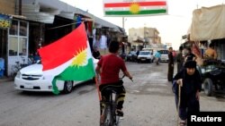 A boy rides a bicycle with the flag of Kurdistan in Tuz Khurmato, Iraq, Sept. 24, 2017. 