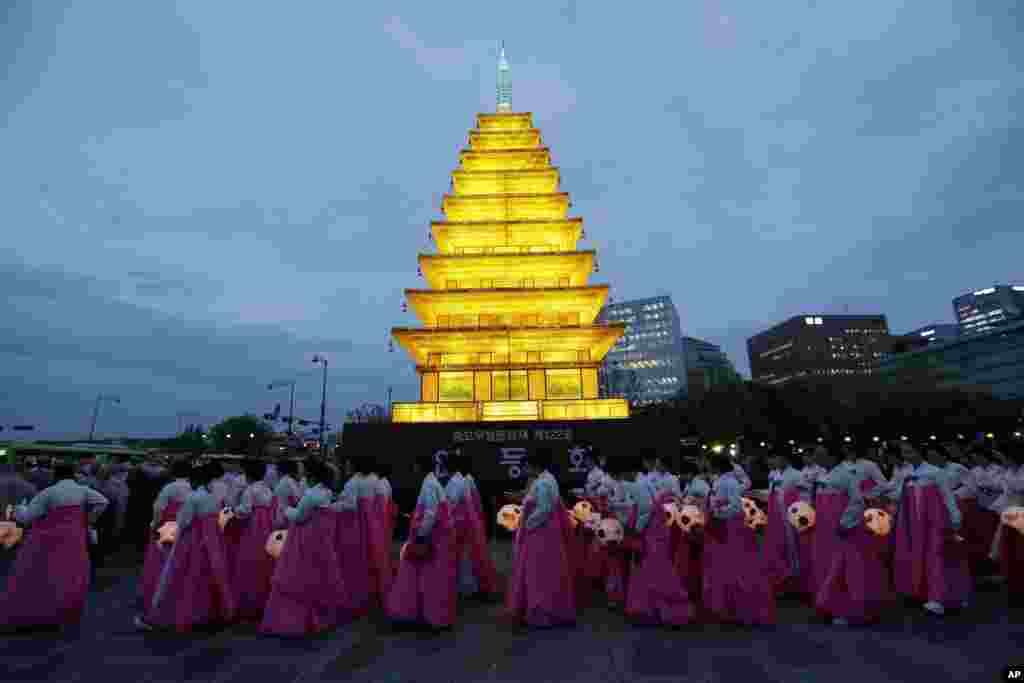 Wearing traditional Korean dress, Buddhist believers holding lanterns walk by a lantern tower in the shape of a Buddhist temple pagoda to celebrate the upcoming Buddha&#39;s birthday on May 25 at the Gwanghwamun Plaza in Seoul, South Korea.