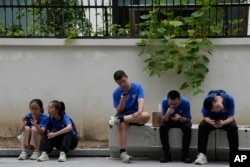 FILE - Youths look at their smartphones on the street in Beijing, Thursday, Aug. 3, 2023. (AP Photo/Ng Han Guan)