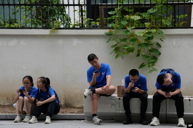 FILE - Youths look at their smartphones on the street in Beijing, Thursday, Aug. 3, 2023. (AP Photo/Ng Han Guan)