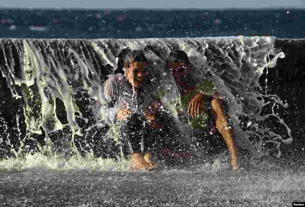 Sepasang muda-mudi tertawa saat gelombang laut menghantam mereka di pantai &#39;El Malecon&#39;, Havana, Kuba.