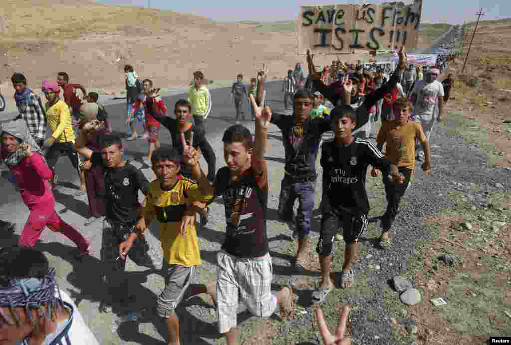 Displaced people from the minority Yazidi sect, who fled the violence in the Iraqi town of Sinjar, flash signs as they take part in a demonstration at the Iraqi-Syrian border crossing in Fishkhabour, Dohuk province, August 13, 2014.