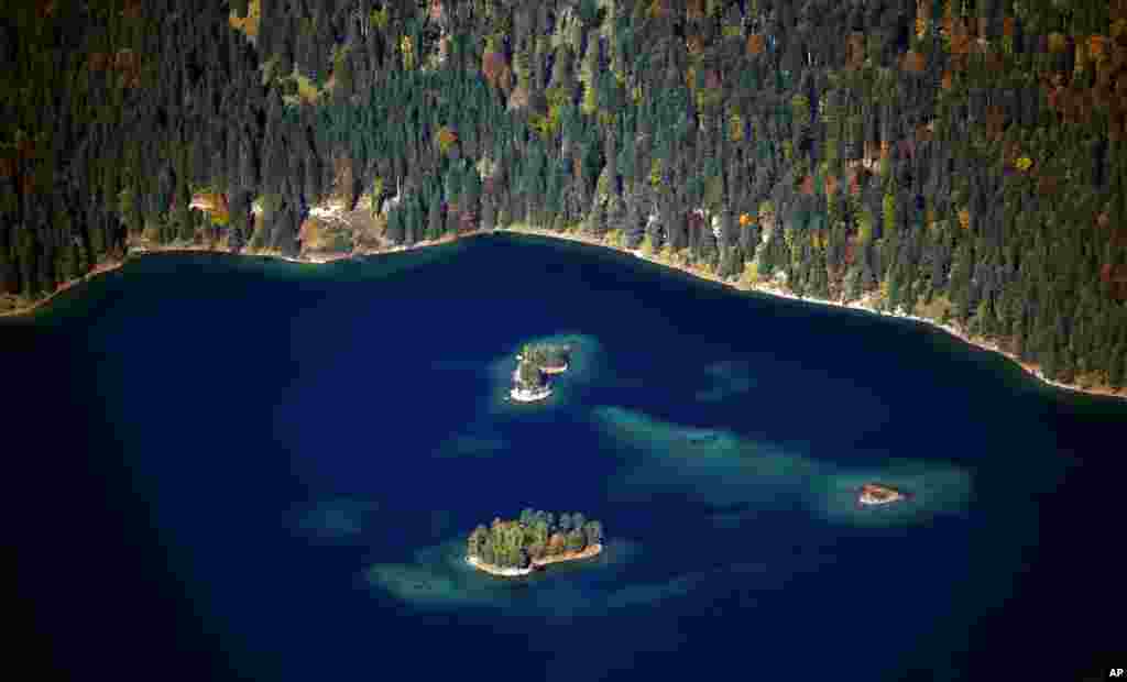 Matahari bersinar di tengah Danau Eibsee yang berwarna biru, yang dikelilingi oleh pohon-pohon yang daunnya mulai berwarna-warni, saat musim gugur di lembah gunung Zugspitze, dekat Garmisch-Partenkirchen, di Jerman selatan.