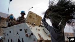 Une jeune fille, avec un bassin plein de balais à vendre sur la tête, passe devant des Casques bleus patrouillant dans les rues de Goma à bord d’une auto blindée des Nations Unies, dans l'est du Congo, 11 juillet 2012. 