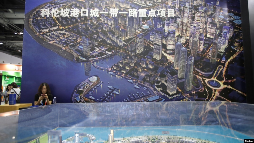 FILE - A woman checks her phone next to a poster promoting a project of the Belt and Road in Colombo, Sri Lanka at China International Fair for Trade in Services in Beijing, China, May 28, 2019.