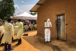 A worker from the World Health Organization decontaminates the doorway of a house on a plot where two cases of Ebola were found, in the village of Mabalako, in eastern Congo, June 17, 2019. Health officials in eastern Congo began offering vaccines.