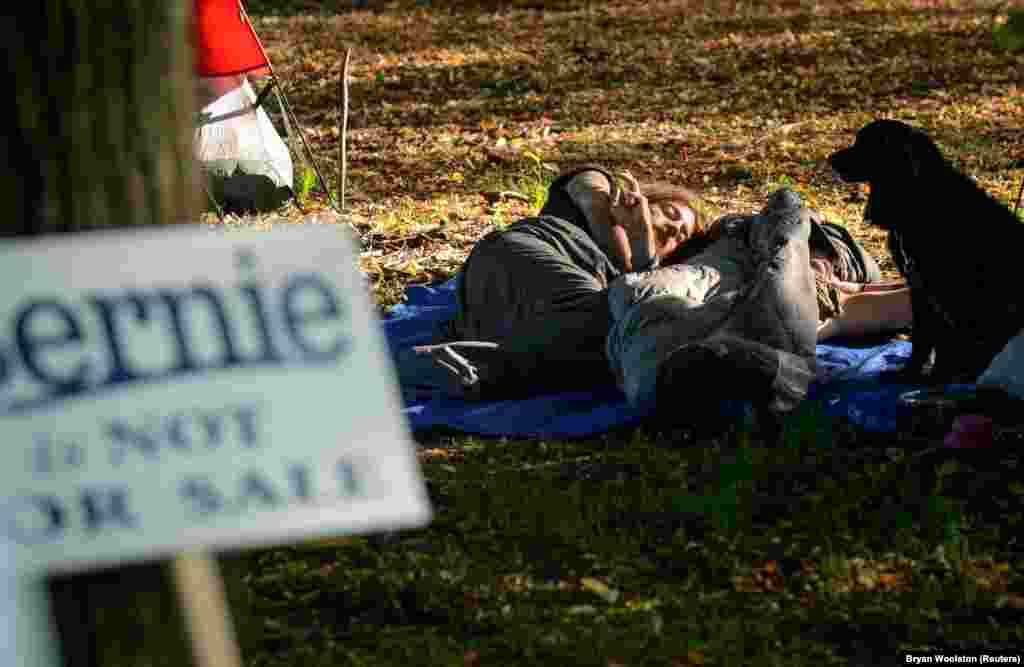 Manifestantes pró-Bernie descansam num jardim e no cartaz desfocado na foto a mensagem diz: "Bernie não está à venda". Filadélfia