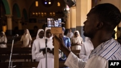 FILE - A man uses a phone to broadcast the traditional Easter Sunday mass live on social media at the Cathedral of the Immaculate Conception in Ouagadougou, Burkina Faso, April 12, 2020. 