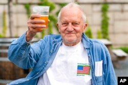 FILE - George Ripley, 72, of Washington holds up his free beer after receiving the J &amp; J COVID-19 vaccine shot, at The REACH at the Kennedy Center in the nation's capital, May 6, 2021.