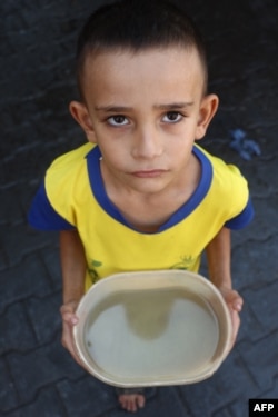 A displaced Palestinian boy carries a plastic container of soup next to a kitchen offering food rations in Deir al-Balah, Gaza Strip, Oct. 17, 2024.