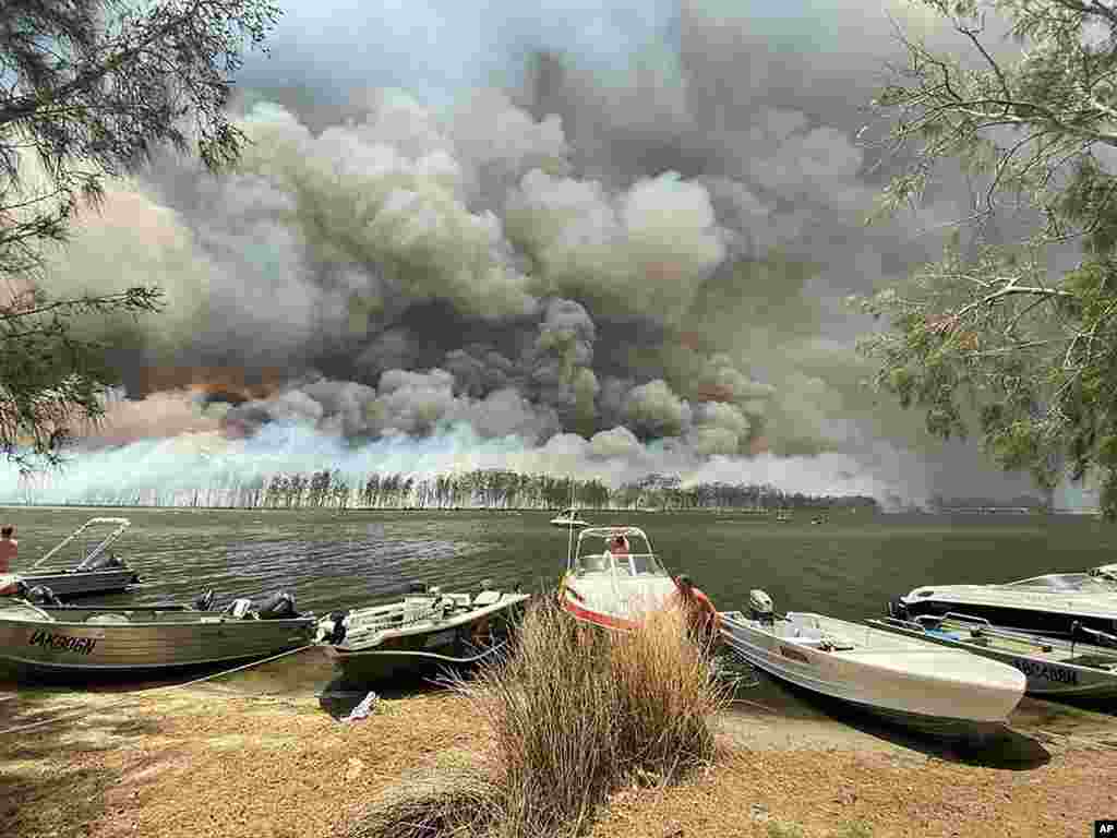 Boats are pulled ashore as smoke and wildfires rage behind Lake Conjola, Australia.