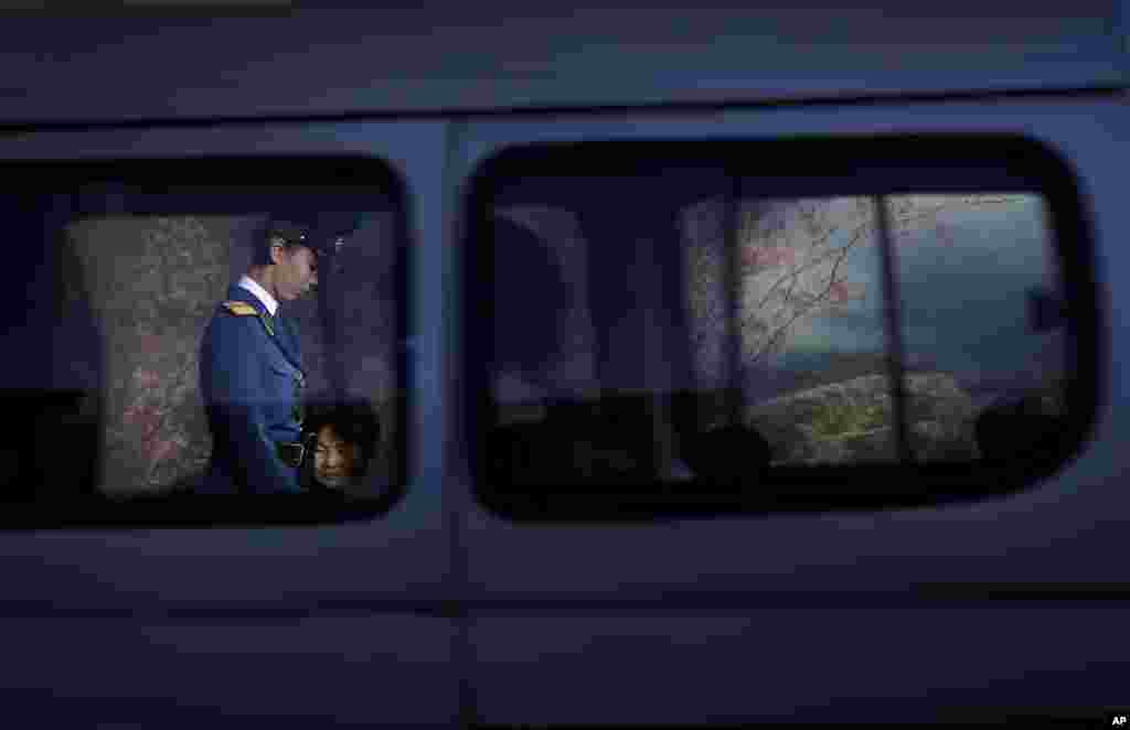 A North Korean traffic police woman is framed by a window of a passing vehicle as she walks past commuters waiting at a bus stop at the end of a workday in Pyongyang.