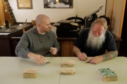 Loren Ackerman (kanan) dan Wali Kota Tenino Wayne Fournier (kiri) menandatangani uang-uang kayu yang dicetak Ackerman dengan alat cetak dari 1890an, di Tenino, Washington, 21 Mei 2020. (Foto: AP)