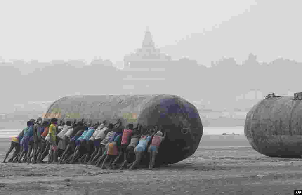 Indian laborers push a pontoon buoy in the banks of the Ganges River as they build floating bridges for the upcoming Hindu festival of Magh Mela, in Allahabad.