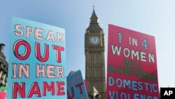 FILE - People hold banners during a demonstration against domestic violence near Big Ben in London, March 5, 2013. 