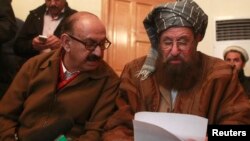 FILE- Maulana Sami ul-Haq (R), one of the Taliban negotiators, and Irfan Siddiqui, a government negotiator, discuss a joint statement before a news conference in Islamabad, Pakistan, Feb. 6, 2014.