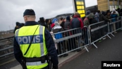 FILE - A police officer keeps guard as migrants arrive at Hyllie station outside Malmo, Sweden. Picture taken Nov. 19, 2015. 