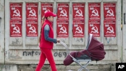 FILE - A woman pushes a stroller past posters advertising the Party of Communists of Moldova, in Chisinau, Moldova, May 28, 2015. 