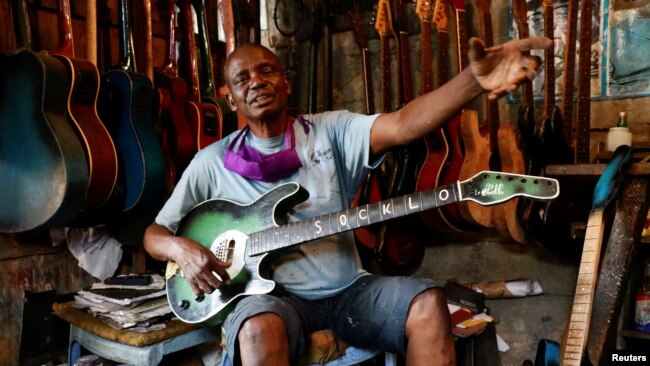 Guitar luthier Misoko Nzalayala Jean-Luther, alias Socklo, 61, gestures while he holds one of his instruments at his workshop in Kinshasa, Democratic Republic of Congo, Oct.18, 2021.