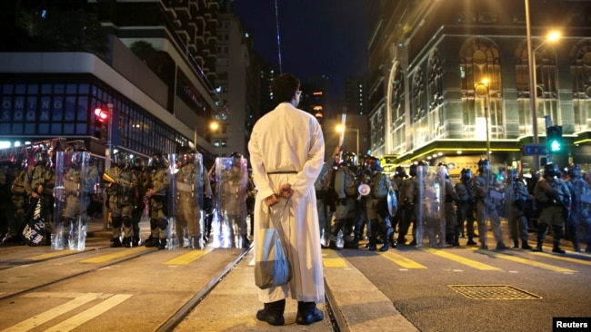 在香港坚尼地城，一名宗教人士站在防暴警察前。(2019年8月4日)