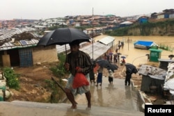 FILE - Rohingya refugees walk along a camp during rain in Cox’s Bazar, Bangladesh, July 25, 2018.