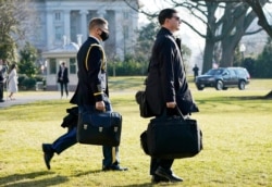 A U.S. military aide, left, carries the "President's emergency satchel," also know as "the football," with the nuclear launch codes, as President Donald Trump walks to board Marine One, Jan. 12, 2021.
