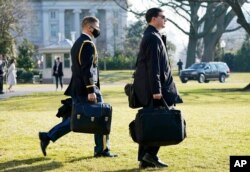 A U.S. military aide, left, carries the "President's emergency satchel," also know as "the football," with the nuclear launch codes, as President Donald Trump walks to board Marine One, Jan. 12, 2021.