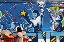 FILE - A resident stands near a mural depicting the famous "Hand of God" goal by former Argentine soccer star Diego Maradona,