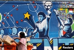 FILE - A resident stands near a mural depicting the famous "Hand of God" goal by former Argentine soccer star Diego Maradona,