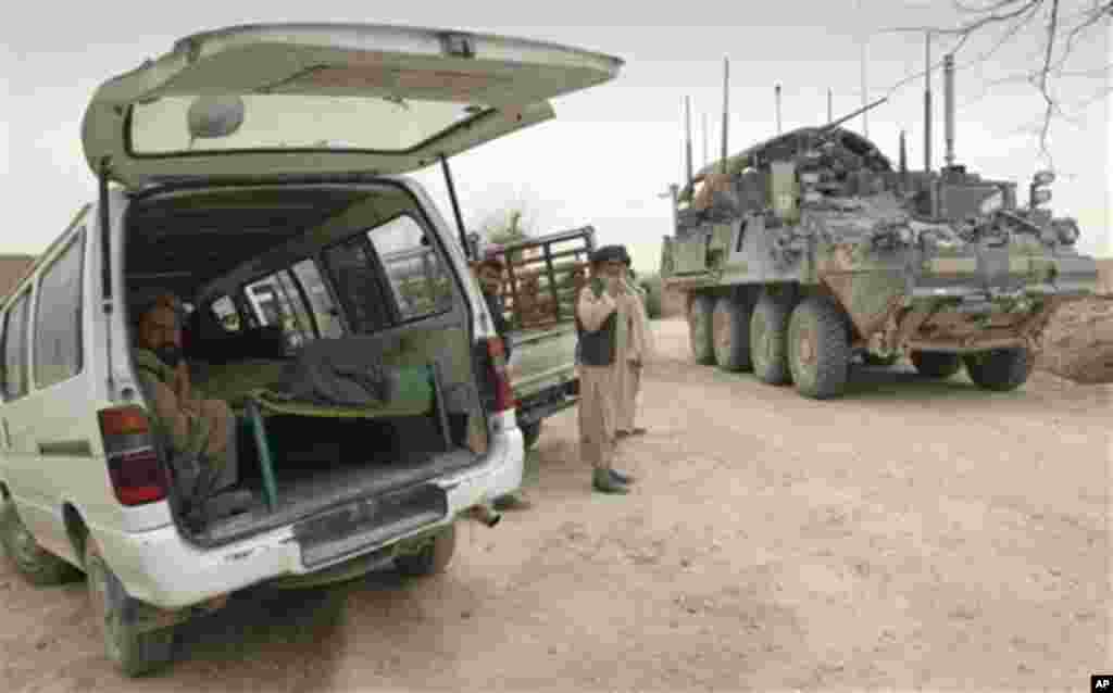 An armored military vehicle from the NATO-led International Security Assistance Force (ISAF) is seen at right, as the covered body of a person who was allegedly killed by a U.S. service member is seen inside a minibus in Panjwai, Kandahar province south o