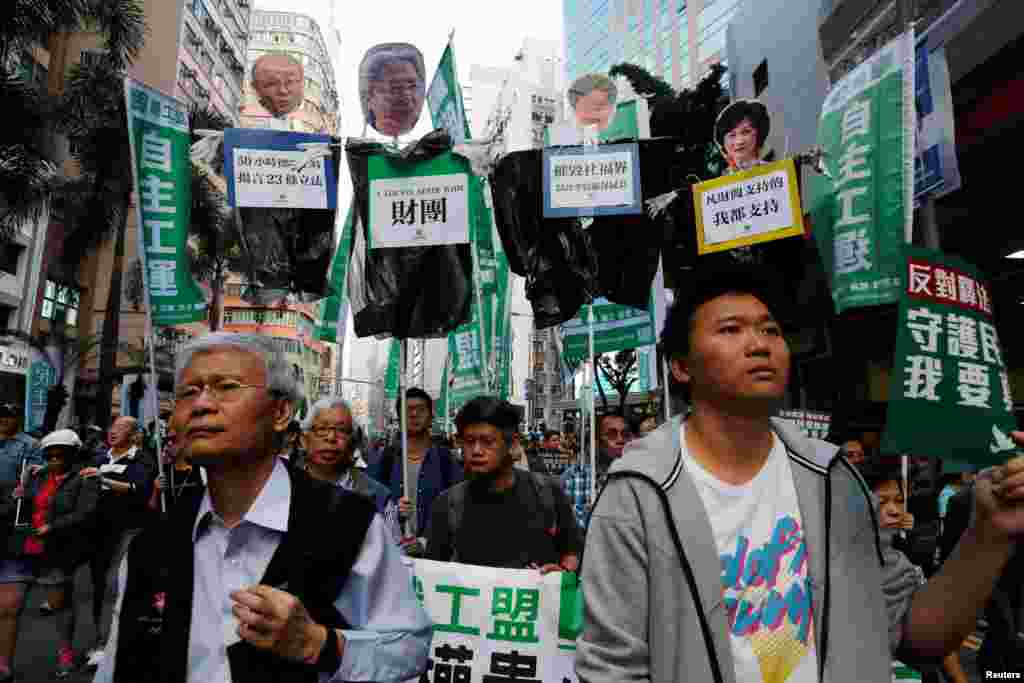 香港示威者举着标语牌：&ldquo;反对释法，撤回复核，守护民选制度，我要真普选&rdquo;，支持被香港政府司法复核，寻求撤销其立法会议员资格的刘小丽、姚松炎、梁国雄及罗冠聪。 还有人批判性地举着四位竞选特首者的头像，下面的标语强调这些候选人支持现有体制或者财团。 （2017年1月1日）