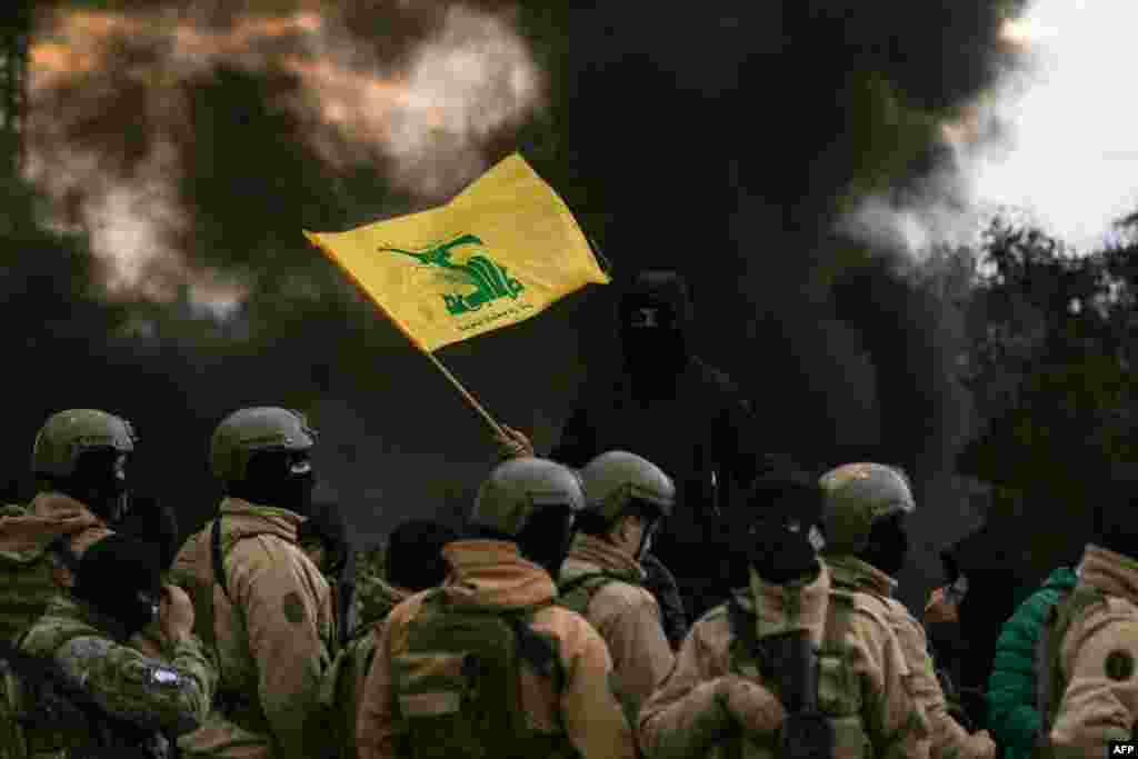 A Hezbollah supporter waves the group&#39;s flag in front of Lebanese army troops, as protesters burn tires to block the road leading to Beirut&#39;s international airport, during a demonstration against statements made by U.S. deputy special envoy for Middle East peace Morgan Ortagus after she met with the country&#39;s president, in Beirut, Lebanon.