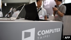 FILE - Visitors stand behind a desk with the Computex logo during Computex 2018, at the Nangang Exhibition Center in Taipei, Taiwan, June 5, 2018.