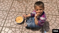 Young Iraqi boy eating rice with tomato sauce. (S. Behn/VOA)