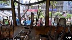 Orang-orang memperhatikan bus yang hangus dibakar oleh para aktivis Partai Nasionalis Bangladesh saat demo di tengah mogok kerja di Dhaka, Minggu, 29 Oktober 2023. (Foto: Munir Uz Zaman /AFP)