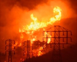 FILE - Flames burn near power lines in Sycamore Canyon in Montecito, Calif., Dec. 16, 2017. As California counties face power shutoffs meant to prevent wildfires, counties with more resources are adapting easier than poorer ones.
