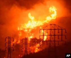FILE - Flames burn near power lines in Sycamore Canyon in Montecito, Calif., Dec. 16, 2017. As California counties face power shutoffs meant to prevent wildfires, counties with more resources are adapting easier than poorer ones.