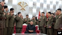 ທ່ານ Kim Jong Un, ຜູ້ນໍາເກົາຫລີເໜືອນັ່ງຢູ່ ແລະມີເຈົ້າໜ້າທີ່ທະຫານຂັ້ນສູງຫ້ອມລ້ອມທ່ານ ຢູ່ໃນພິທີ “Paektusan” ມອບປືນສັ້ນຂອງທ່ານ ໃຫ້ແກ່ເຂົາເຈົ້າຢູ່ໃນນະຄອນພຽງຢາງ, ວັນທີ 26 ກໍລະກົດ, 2020. (ພາບສະໜອງໃຫ້ໂດຍລັດຖະບານເກົາຫລີເໜືອ)