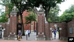 FILE - In this Aug. 13, 2019, file photo, pedestrians walk through the gates of Harvard Yard at Harvard University in Cambridge, Mass. Harvard and the Massachusetts Institute of Technology filed a federal lawsuit challenging the new international visa rule. 