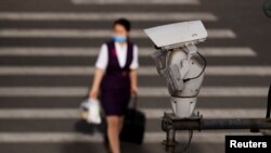FILE - A CCTV security surveillance camera overlooks a street as a woman walks past following the spread of the novel coronavirus disease in Beijing, China, May 11, 2020. 