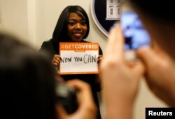 FILE - A woman poses for photos while holding a placard with her thoughts on health care at the White House Youth Summit on the Affordable Care Act in Washington, Dec. 4, 2013.