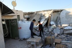 Boys stand near a damaged house after shells fell on a residential area, in Abu Slim district, south of Tripoli, Libya, Feb. 28, 2020.