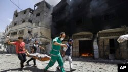 Petugas medis Palestina membawa korban sambil berlari melewati gedung yang terbakar di Shijaiyah, Gaza City di Jalur Gaza utara, Minggu, 20 Juli 2014.