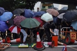 Protesters hide behind umbrellas as they form a barricade to block a road in Hong Kong, Oct. 4, 2019.