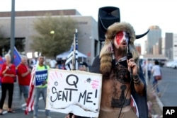 FILE - In this Nov. 5, 2020 photo, Jacob Anthony Chansley, a QAnon believer, speaks to a crowd of President Donald Trump supporters outside of the Maricopa County Recorder's Office where votes in the general election were being counted, in Phoenix.